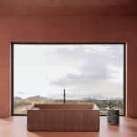 Wooden freestanding bathtub facing a large floor-to-ceiling window with a desert landscape outside.