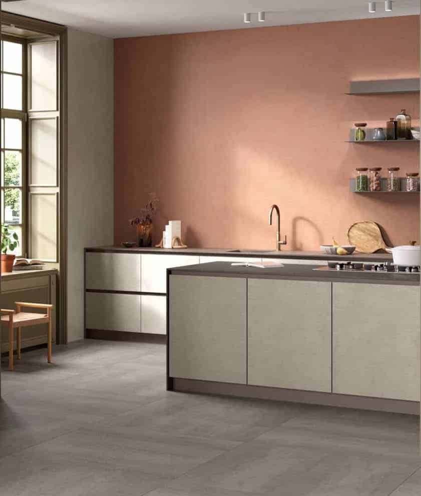 Modern kitchen with pale cabinets, pink accent wall, and a central island; window on the left fills the space with light.