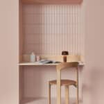 Pastel pink study alcove with tiled walls, a wooden desk, a magazine, mug, and a small black lamp in the corner of the desk.